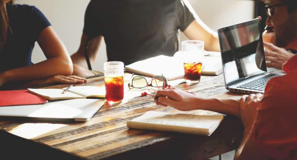 people sitting around a table with a laptop, journals, books and beverages