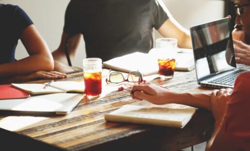 people sitting around a table with a laptop, journals, books and beverages